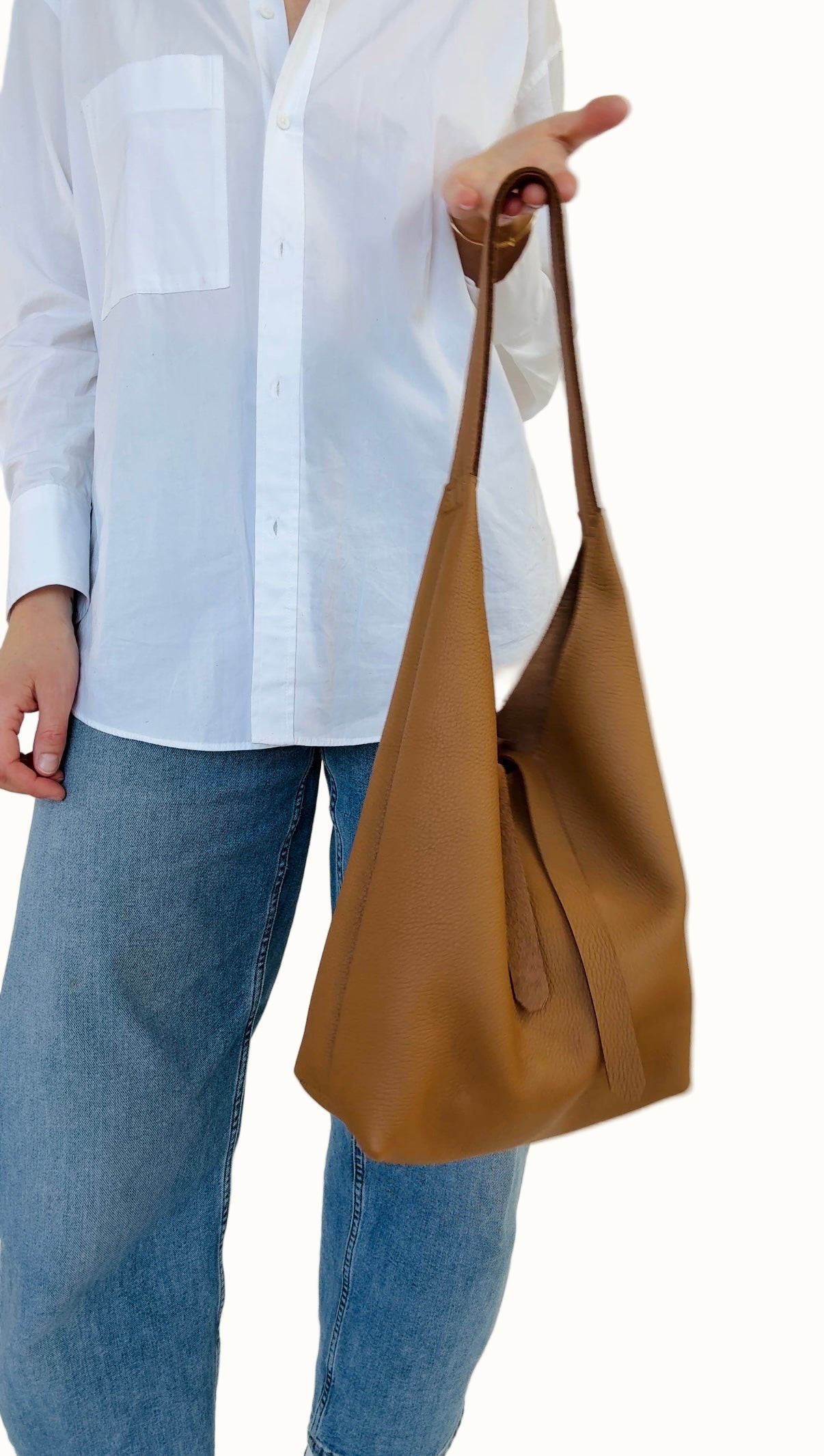 A person holding a brown leather shoulder bag with a light-colored shirt and blue jeans.