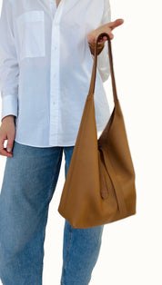 A person holding a brown leather shoulder bag with a light-colored shirt and blue jeans.