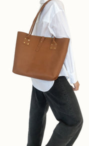 Person wearing a brown leather tote bag over one shoulder against a white background