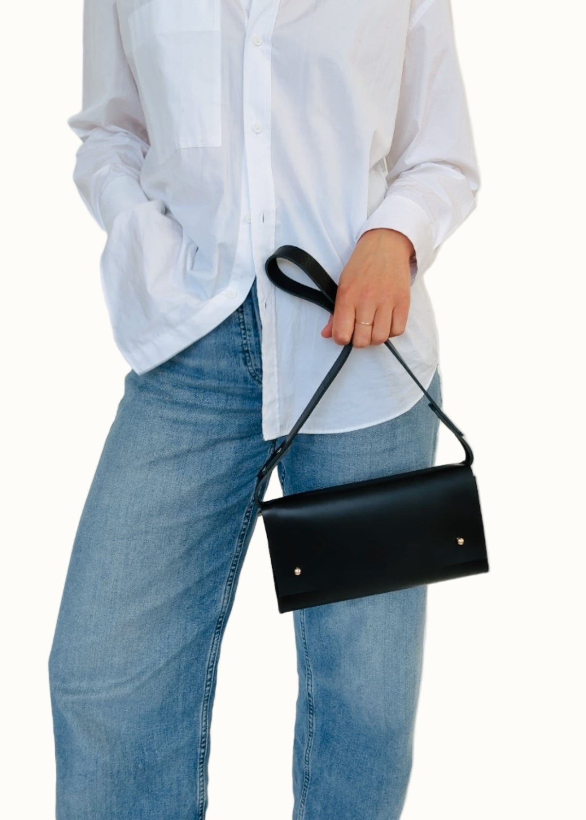A person wearing a white shirt and blue jeans, holding a black shoulder bag with a strap.