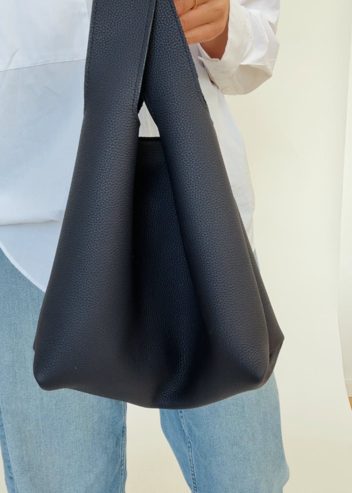 A person holding a dark navy mini tote bag with a shoulder strap.