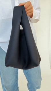 A person holding a dark navy mini tote bag with a shoulder strap.