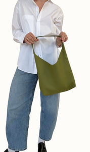 A person wearing a white shirt and blue jeans is holding a green shoulder bag over their shoulder.