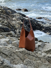 Brown leather handbag on a rocky beach with ocean waves in the background
