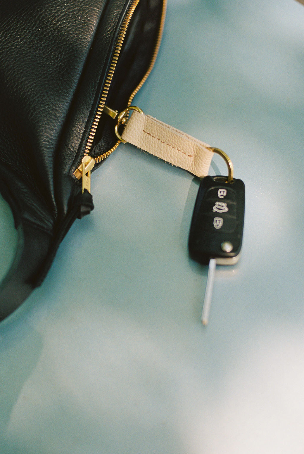 Car key with remote on a black leather bag against a light blue background