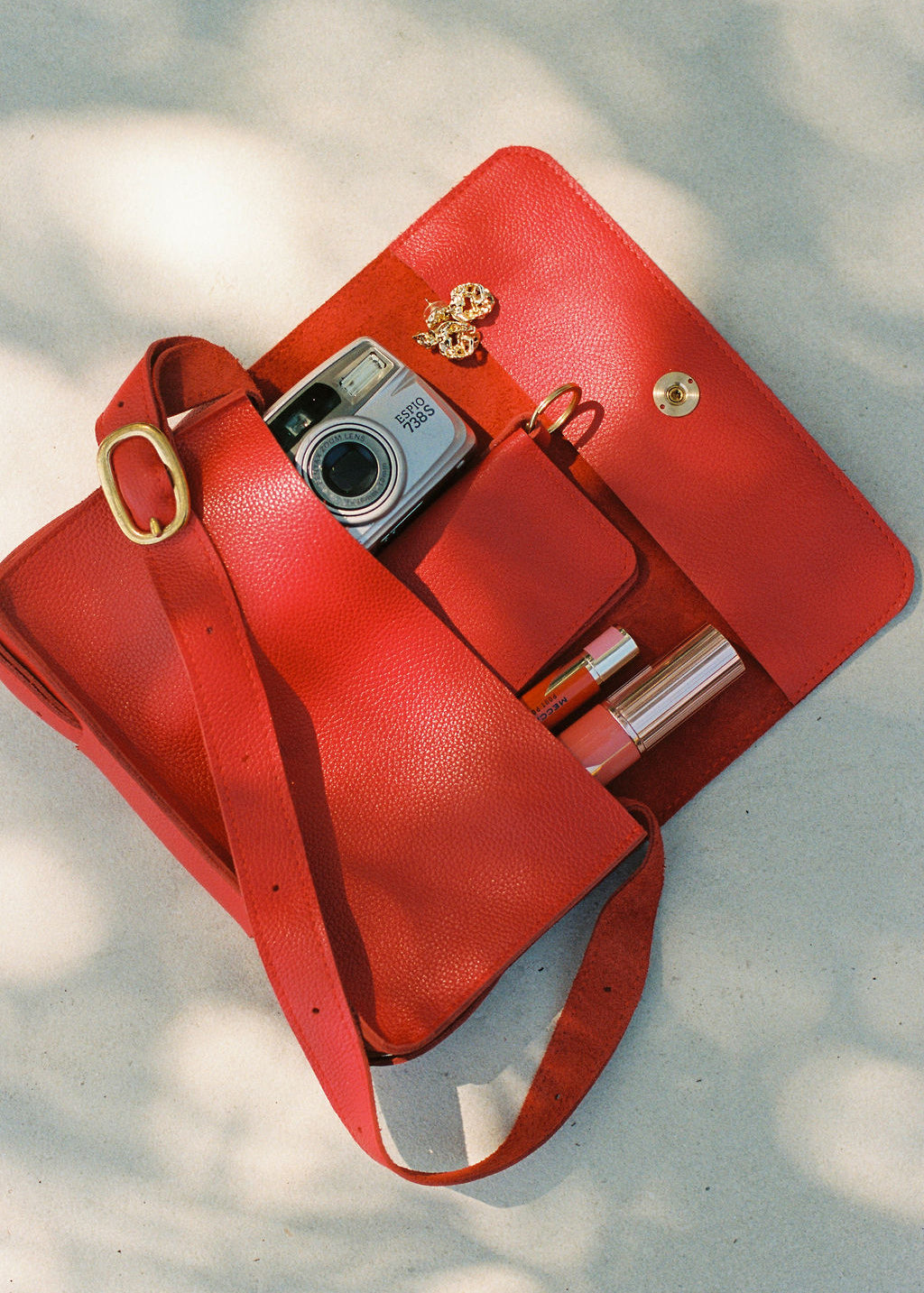 Red handbag with a camera and lipsticks on a light background