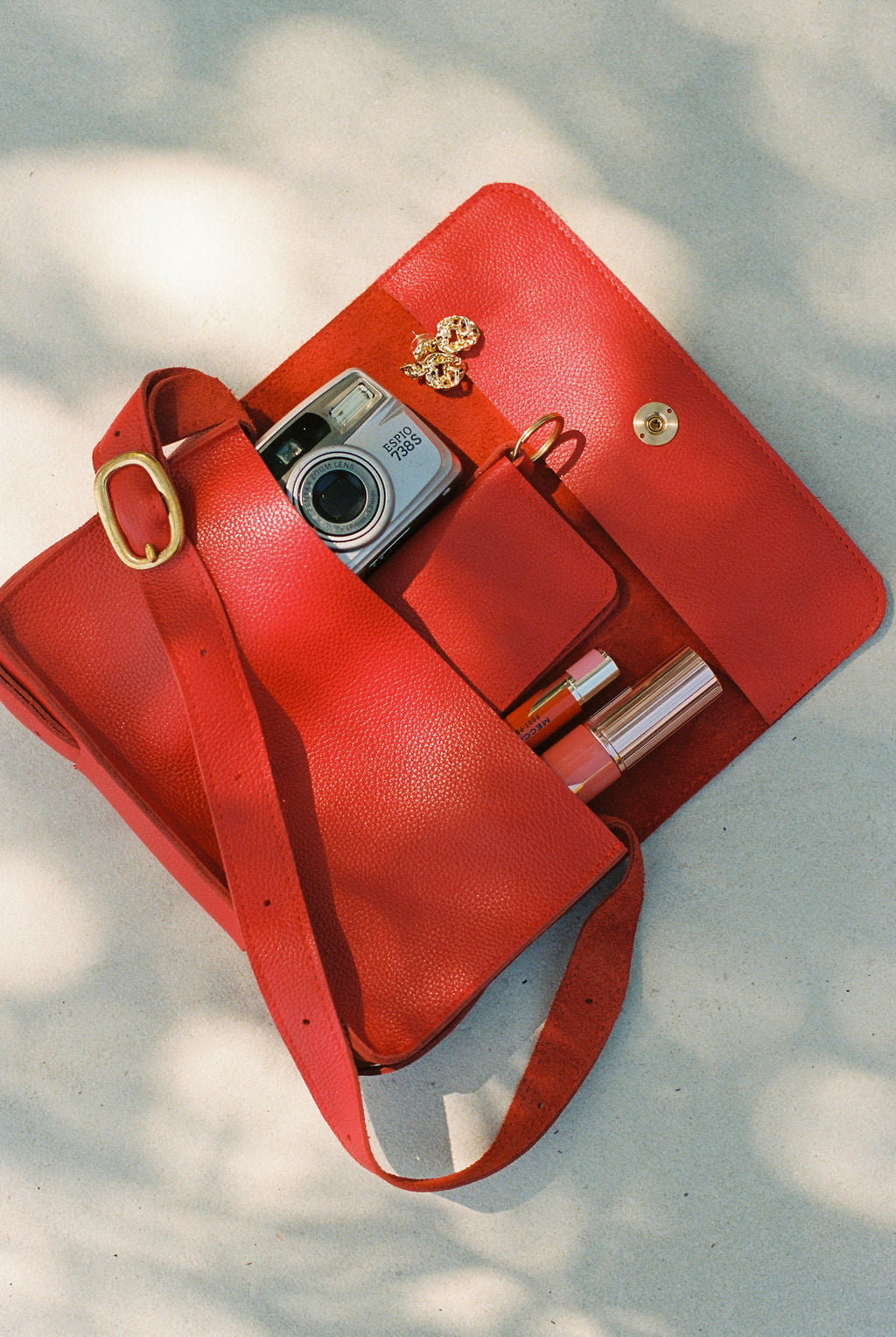 Red handbag with a camera and lipsticks on a light background