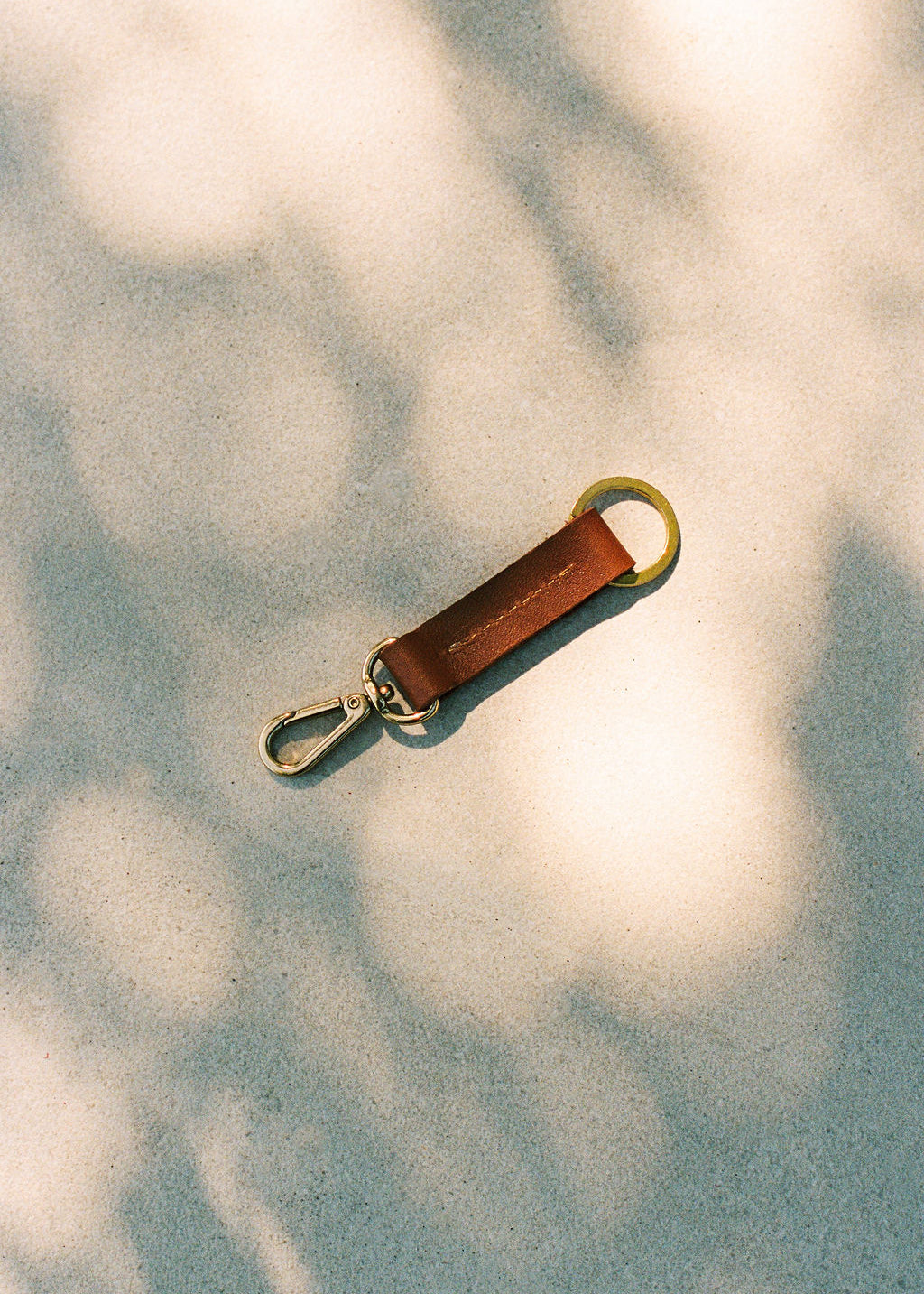 Brown leather keychain with gold clasp on a textured surface