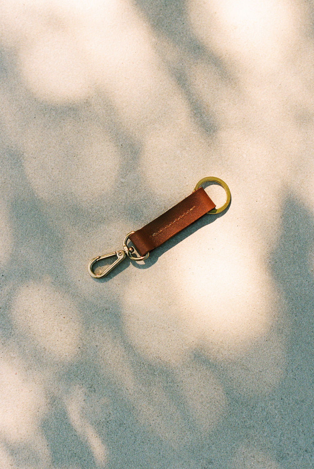 Brown leather keychain with gold clasp on a textured surface