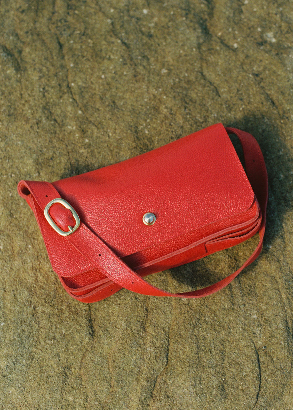 Red leather handbag on a sandy surface