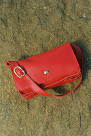 Red leather handbag on a sandy surface
