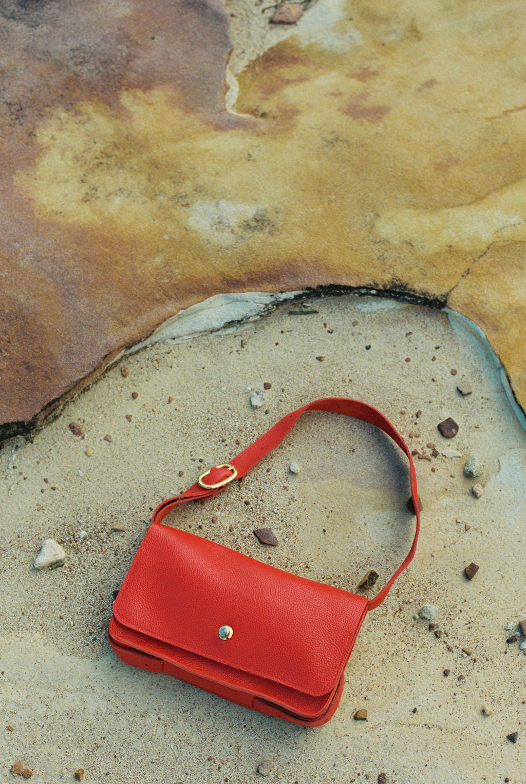Red handbag on a textured surface with pebbles